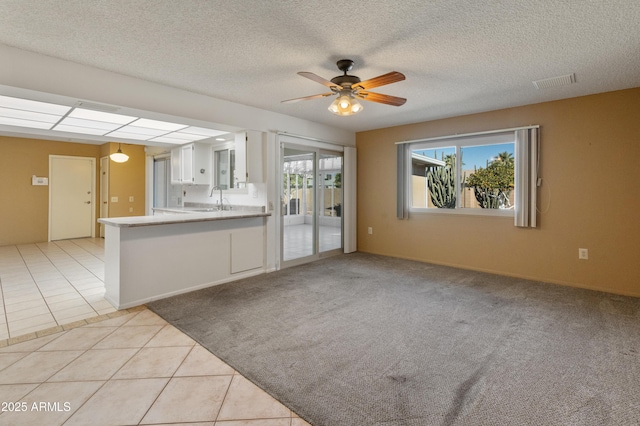 unfurnished living room with ceiling fan, sink, a textured ceiling, and light tile patterned flooring