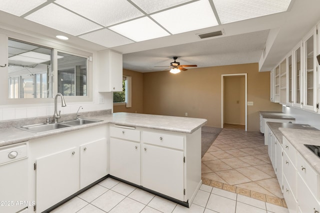 kitchen featuring kitchen peninsula, white dishwasher, sink, white cabinets, and light tile patterned floors