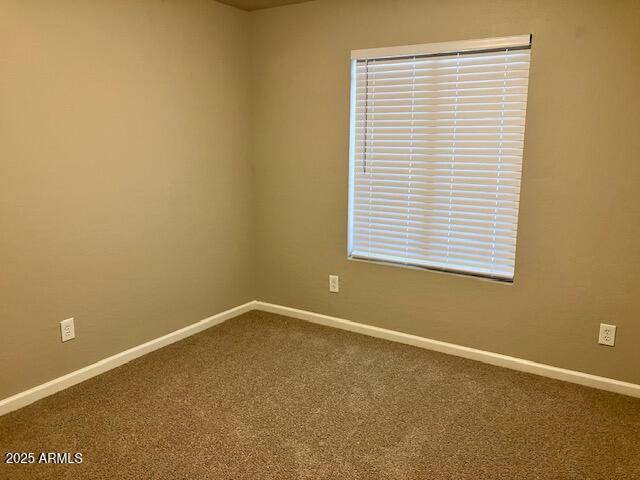 spare room with baseboards and dark colored carpet