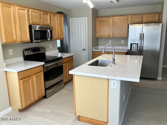 kitchen featuring light stone countertops, a sink, baseboards, stainless steel appliances, and an island with sink
