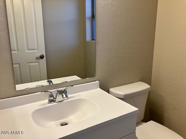 half bath featuring vanity, a textured wall, and toilet