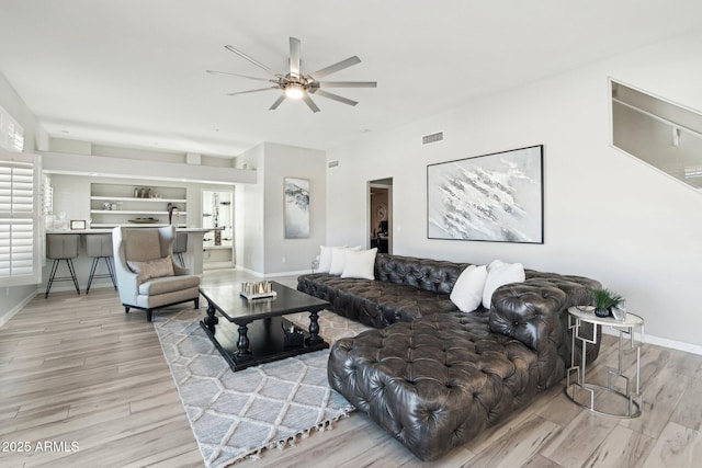 living room featuring ceiling fan, light wood-type flooring, visible vents, and baseboards