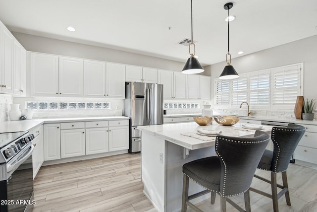 kitchen with sink, hanging light fixtures, stainless steel appliances, a center island, and white cabinets