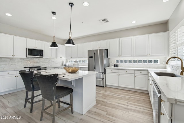 kitchen with appliances with stainless steel finishes, sink, a kitchen island, and white cabinets