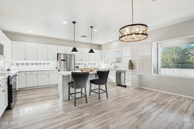 kitchen featuring light countertops, appliances with stainless steel finishes, white cabinetry, light wood-type flooring, and a kitchen bar