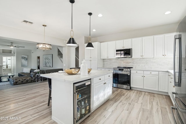 kitchen featuring pendant lighting, appliances with stainless steel finishes, white cabinets, a kitchen island, and beverage cooler