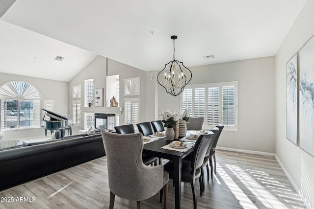 dining space featuring lofted ceiling, light wood-type flooring, a chandelier, and a multi sided fireplace