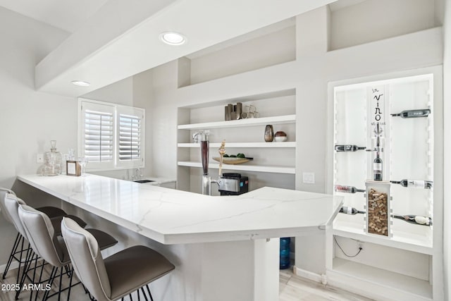 kitchen featuring a breakfast bar, light stone counters, light hardwood / wood-style floors, built in shelves, and kitchen peninsula