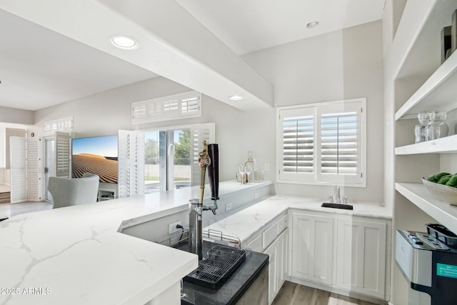 kitchen with sink, light hardwood / wood-style flooring, light stone counters, white cabinets, and kitchen peninsula