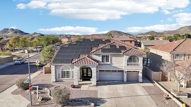 mediterranean / spanish-style house with an attached garage, roof mounted solar panels, a mountain view, fence, and driveway