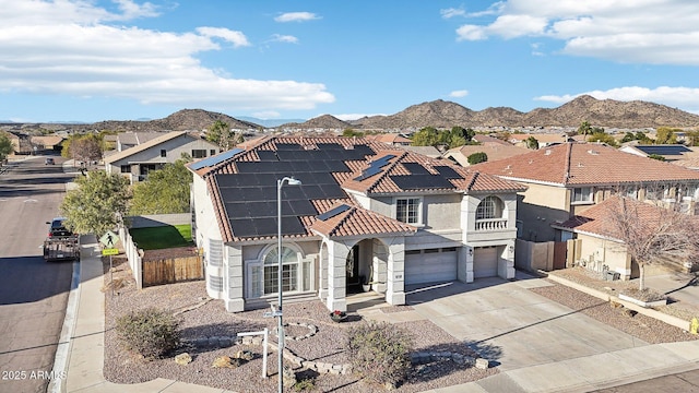 view of front of property featuring roof mounted solar panels, fence, a mountain view, a residential view, and driveway