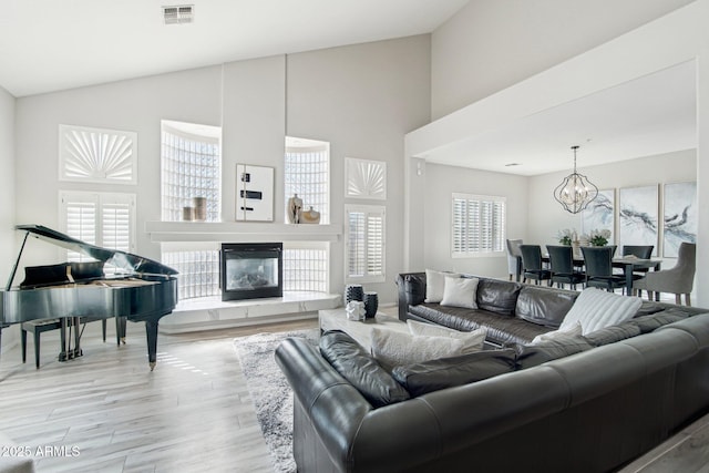 living area featuring visible vents, a chandelier, a glass covered fireplace, wood finished floors, and high vaulted ceiling