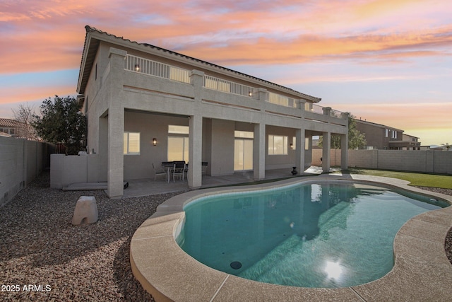 back house at dusk with a fenced in pool and a patio area