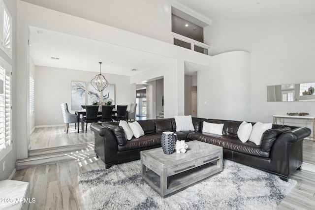 living room with a chandelier, light wood-style flooring, visible vents, a towering ceiling, and baseboards