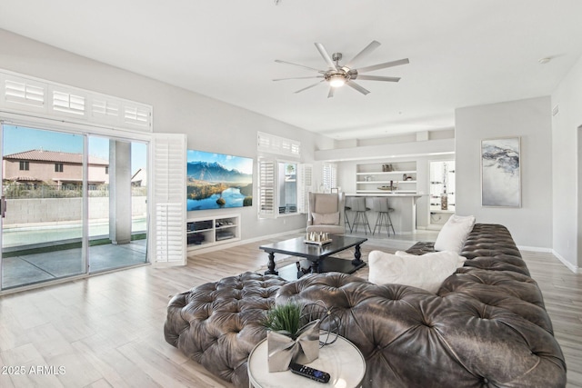 living area featuring a ceiling fan, plenty of natural light, baseboards, and wood finished floors