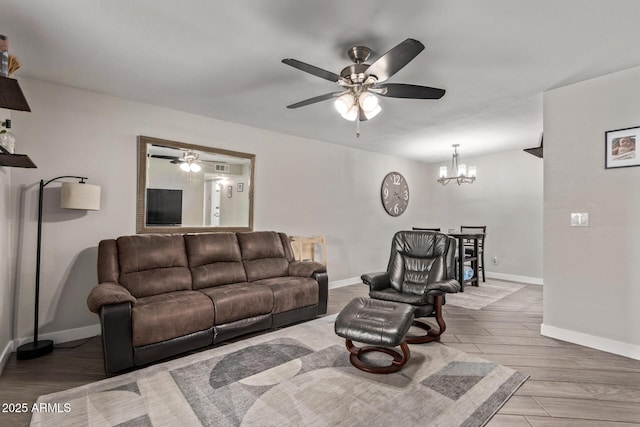 living area featuring ceiling fan with notable chandelier, baseboards, and wood finished floors