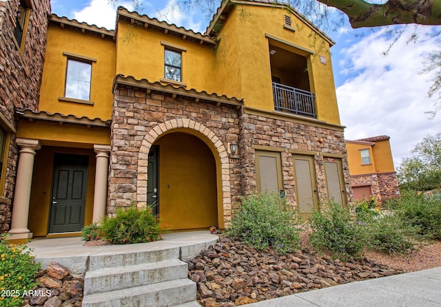 view of front of house featuring a balcony, stone siding, and stucco siding