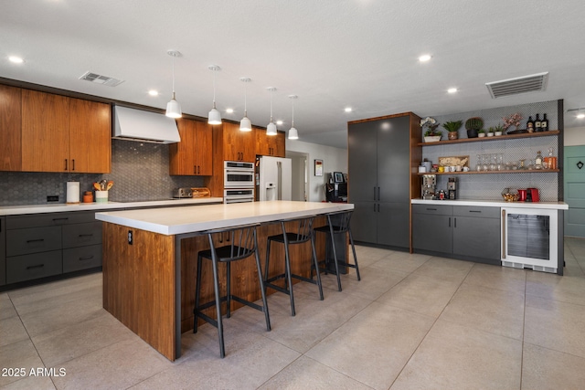 kitchen featuring a kitchen breakfast bar, a center island, white fridge with ice dispenser, decorative light fixtures, and wall chimney exhaust hood