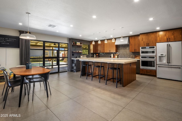 kitchen with wall chimney range hood, a center island, pendant lighting, and high end white fridge