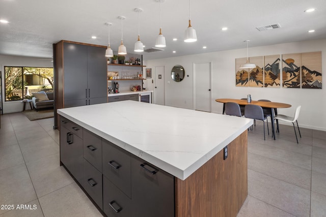 kitchen with light stone counters, a kitchen island, hanging light fixtures, and light tile patterned floors