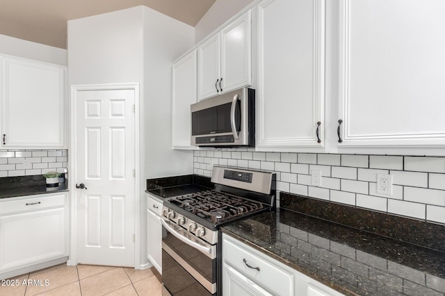 kitchen with appliances with stainless steel finishes, tasteful backsplash, white cabinets, dark stone countertops, and light tile patterned flooring