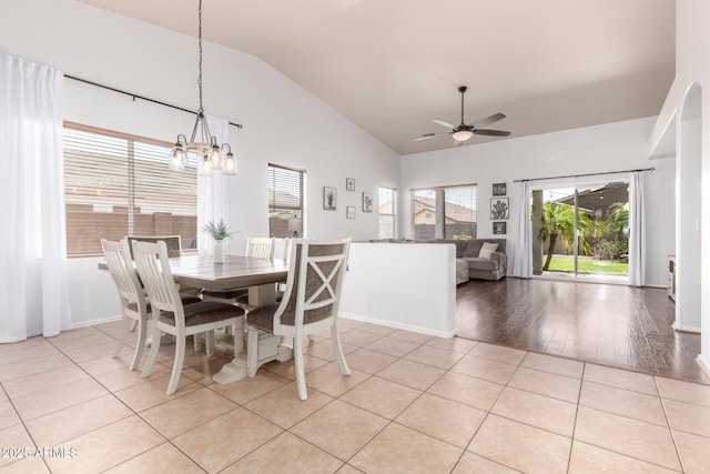 dining room featuring baseboards, ceiling fan with notable chandelier, light tile patterned floors, and high vaulted ceiling