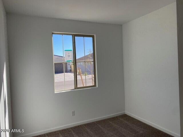 unfurnished room featuring dark colored carpet and baseboards