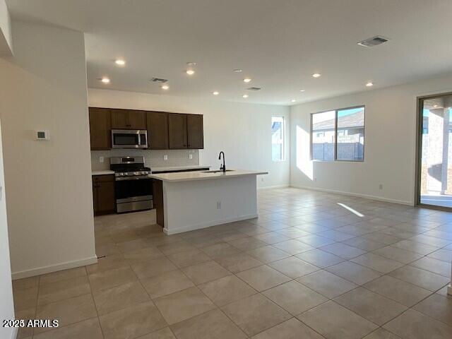 kitchen featuring visible vents, open floor plan, decorative backsplash, appliances with stainless steel finishes, and a sink