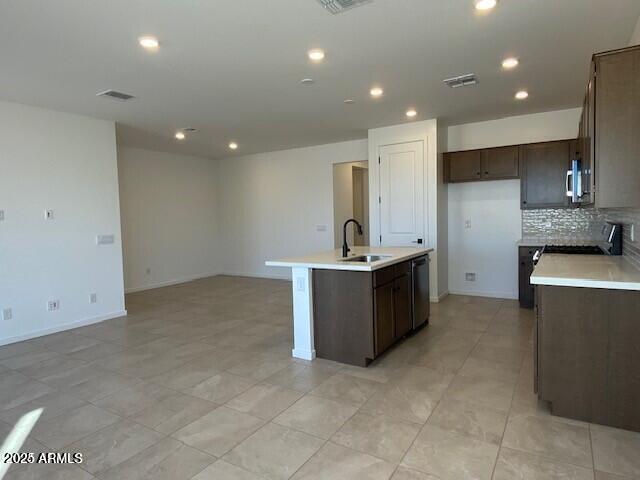 kitchen with visible vents, an island with sink, a sink, light countertops, and dark brown cabinets