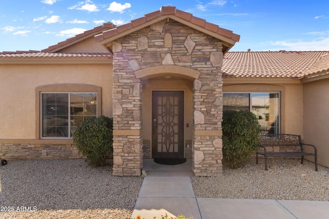 doorway to property featuring a tile roof, stone siding, and stucco siding