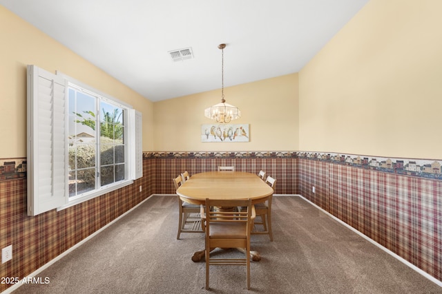 carpeted dining room featuring visible vents, an inviting chandelier, wainscoting, and wallpapered walls