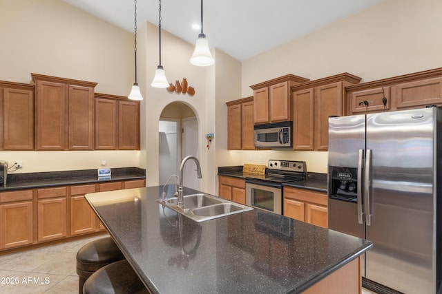 kitchen featuring brown cabinets, arched walkways, appliances with stainless steel finishes, and a sink