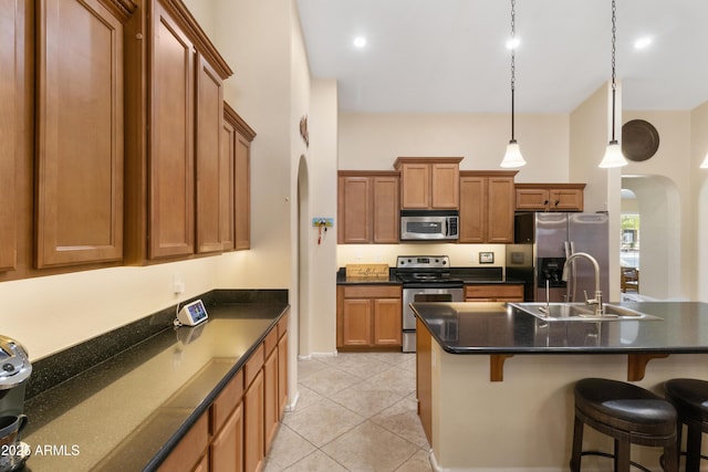 kitchen with a sink, arched walkways, appliances with stainless steel finishes, a breakfast bar area, and brown cabinetry