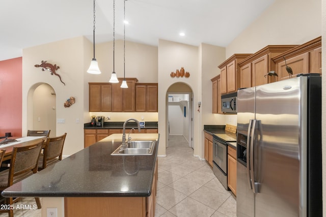 kitchen with a sink, stainless steel appliances, arched walkways, and dark countertops