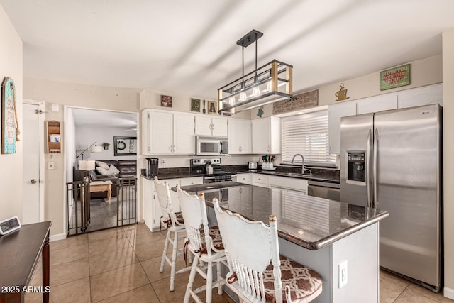 kitchen with sink, appliances with stainless steel finishes, decorative light fixtures, a kitchen island, and white cabinetry