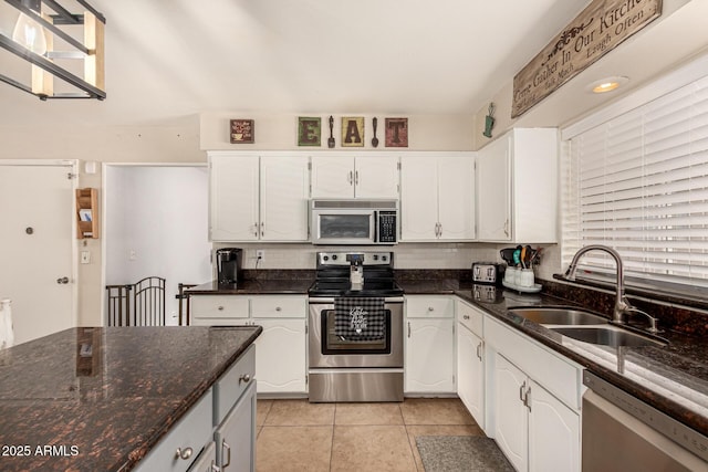 kitchen with dark stone counters, stainless steel appliances, sink, white cabinetry, and light tile patterned flooring