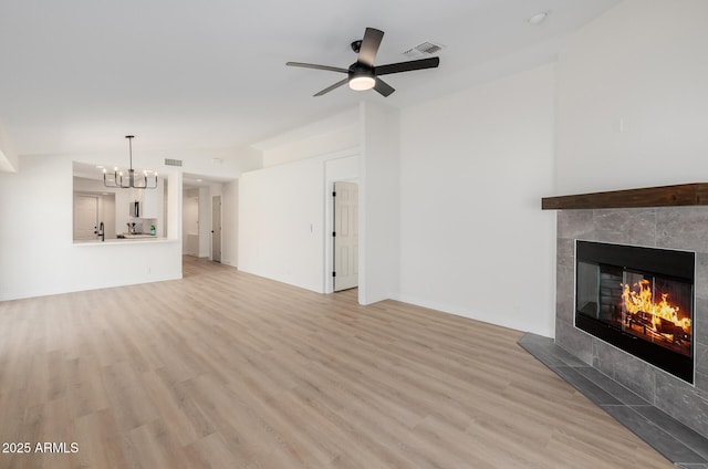 14239 N Edgeworth Dr Unit A, Fountain Hills, AZ 85268 - unfurnished living room featuring light wood-style flooring, a tiled fireplace, a chandelier, and a ceiling fan