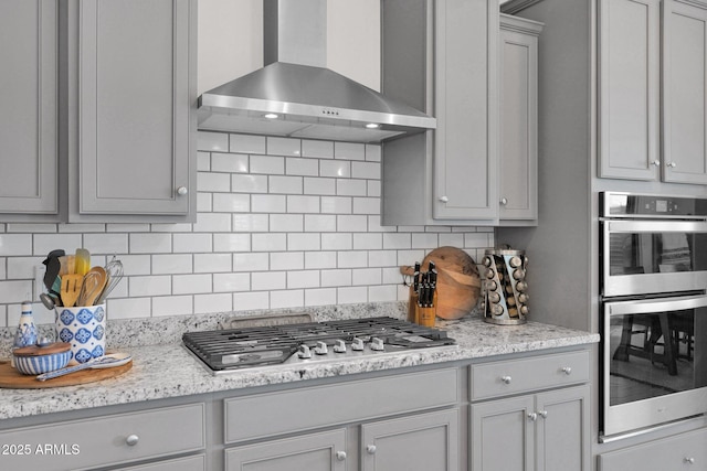 kitchen featuring decorative backsplash, appliances with stainless steel finishes, gray cabinetry, and wall chimney exhaust hood