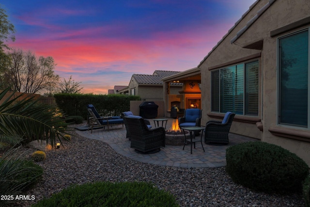 patio terrace at dusk featuring an outdoor fireplace and a fire pit