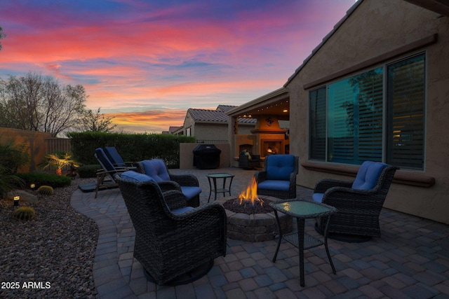 patio terrace at dusk with exterior fireplace, a fire pit, and area for grilling