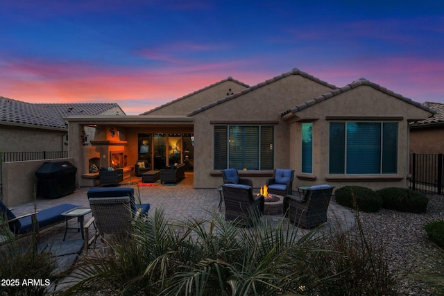 back house at dusk featuring a patio and an outdoor living space with a fireplace