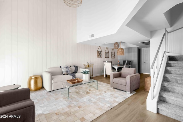 living room with light wood-type flooring, a high ceiling, and wooden walls