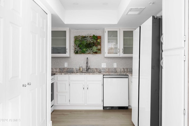 kitchen with white cabinets, sink, light wood-type flooring, tasteful backsplash, and dishwashing machine