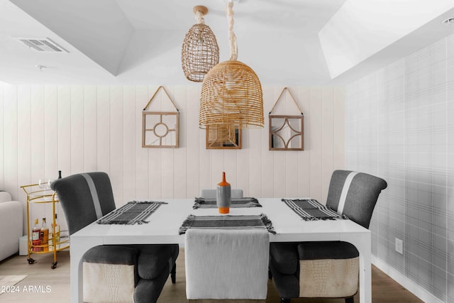 dining room featuring hardwood / wood-style floors, wooden walls, and vaulted ceiling