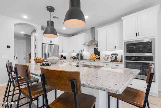 kitchen featuring sink, light stone countertops, wall chimney range hood, and stainless steel appliances