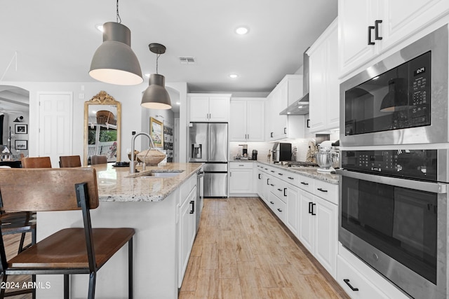 kitchen with appliances with stainless steel finishes, light stone counters, sink, white cabinets, and light hardwood / wood-style floors