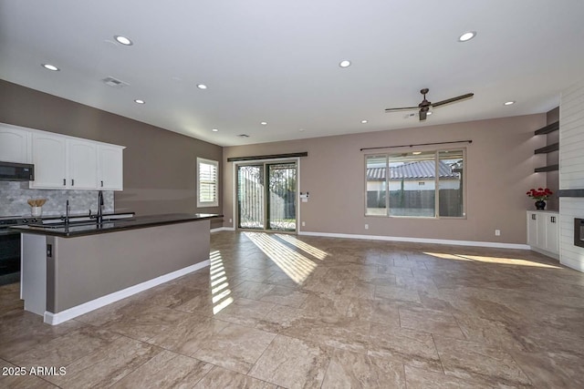 kitchen with sink, white cabinetry, backsplash, a kitchen island with sink, and a fireplace