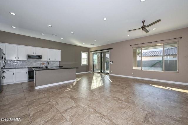 kitchen featuring stainless steel fridge, white cabinetry, stove, tasteful backsplash, and an island with sink