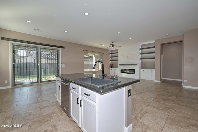 kitchen featuring sink, dishwasher, a fireplace, an island with sink, and white cabinets