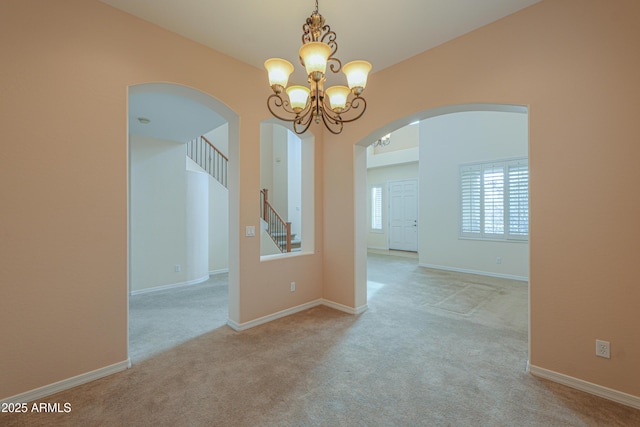 unfurnished room featuring arched walkways, carpet flooring, baseboards, stairway, and an inviting chandelier